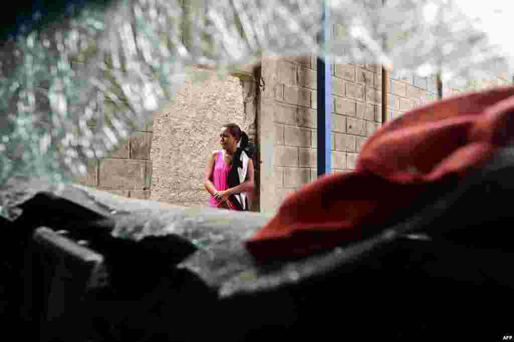 A woman stands next to a damaged car at a supermarket parking bay in Valencia, Carabobo State, Venezuela, the day after anti-government protesters looted stores, set fire to cars and clashed with police.