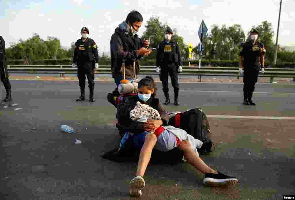 A woman holding a child sits on a motorway surrounded by police in Lima, Peru, April 18, 2020. Peruvians who were stranded in Lima during an ongoing quarantine to halt the spread of the coronavirus make their way to San Martin and other parts of the country.
