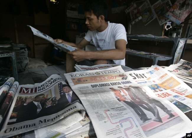 Penjaja koran membaca koran sambil menunggu pelanggan di Jakarta, 10 November 2010. (Foto: AP)