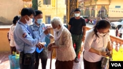 Cambodian authorities perform a temperature check on an elderly woman before entering the pagoda to celebrate Khmer New Year, Phnom Penh, Cambodia, April 14, 2020. (Hean Socheata/VOA Khmer) 