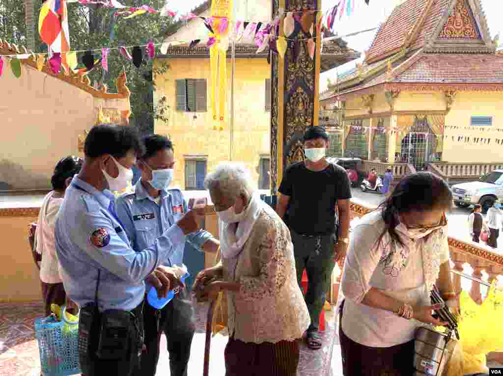 Cambodian authorities perform a temperature check on an elderly woman before entering the pagoda to celebrate Khmer New Year, Phnom Penh, Cambodia, April 14, 2020. (Hean Socheata/VOA Khmer)