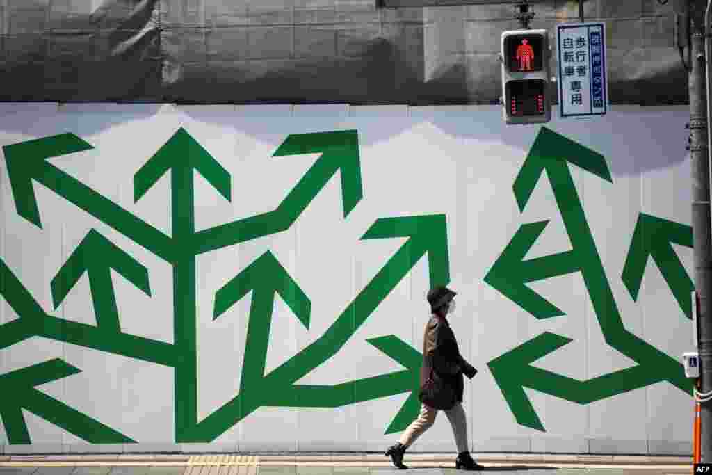 A pedestrian walks past decorated paneling along a street in Tokyo, Japan.