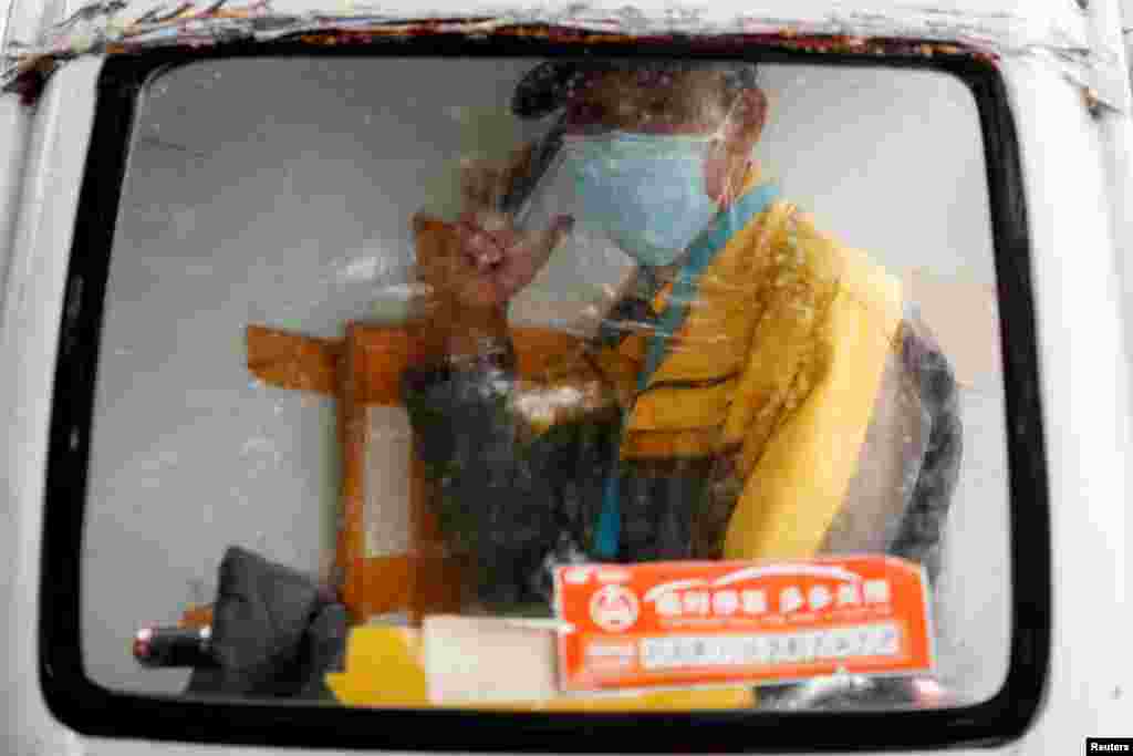 A delivery driver speaks on the phone as he sits in the cabin of his electric delivery vehicle on a rainy day following an outbreak of the coronavirus disease, in Beijing, China.