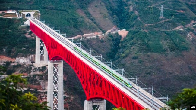 In this photo released by Xinhua News Agency, an electric multiple unit (EMU) train of the China-Laos Railway crosses a major bridge over the Yuanjiang River in southwestern China's Yunnan Province, Dec. 3, 2021.