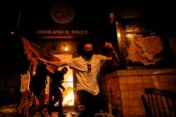 Protesters react as they set fire to the entrance of a police station in Minneapolis, Minnesota.