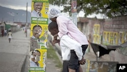 Man carries woman with cholera symptoms past campaign posters in Port-au-Prince (file photo)