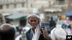 A Yemeni man, right, uses his mobile phone to take photos of his friend as they gather near the historical site of Bab al-Yemen in the the old city of Sana'a, Yemen, Nov. 14, 2012.