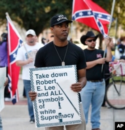 FILE – A man holds a sign during a rally led by the Take 'em Down Coalition, as confederate heritage supporters bear confederate flags nearby in front of City Hall in New Orleans, Dec. 10, 2015. Backlash has stalled work to remove Confederate monuments in New Orleans.