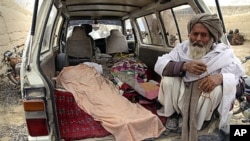 An elderly Afghan man sits in a minivan next to the covered body of a person allegedly shot dead by a U.S. service member in Panjwai, Kandahar province, Afghanistan, Sunday, March 11, 2012.