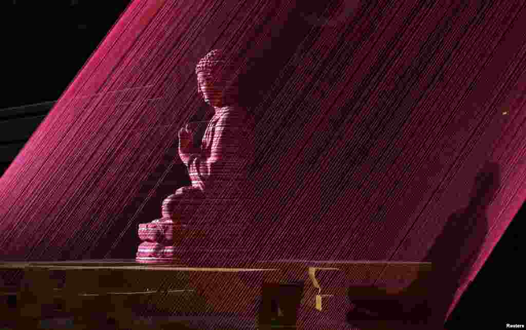 A Buddha sculpture is seen through red strings, which is part of artwork on display at a shopping mall in Beijing. The artwork, made by Chinese sculptor Yang Tao, is comprised of a total of 628 red strings and is about 70 meters in height.