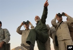 FILE - Photo by the government-controlled Syrian Central Military Media shows Iran's Army Chief of Staff Maj. Gen. Mohammad Bagheri, with binoculars, as he visits senior Iranian military officers in the northern province of Aleppo, Syria, Oct. 17, 2017.