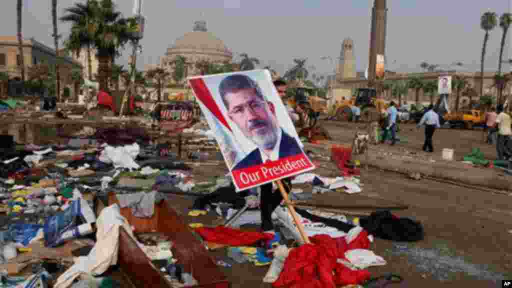 An Egyptian carries a poster of Egypt's ousted President Morsi among debris from a protest camp in Nahda Square, Thursday, Aug. 15, 2013.