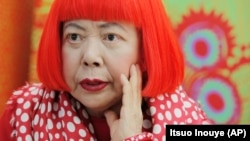 In this photo taken Wednesday, August 1, 2012, Japanese artist Yayoi Kusama wears a bright red wig and a Louis Vuitton polka dot scarf. Her art is known for its colorful use of dots. (AP Photo/Itsuo Inouye)