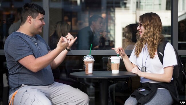Sign language interpretation major,student Nikolas Carapellatti (L) signs with deaf Gallaudet University student Rebecca Witzofsky outside the first US Starbucks café staffed by employees who are partially or fully deaf and capable of communicating in American Sign Language. AFP