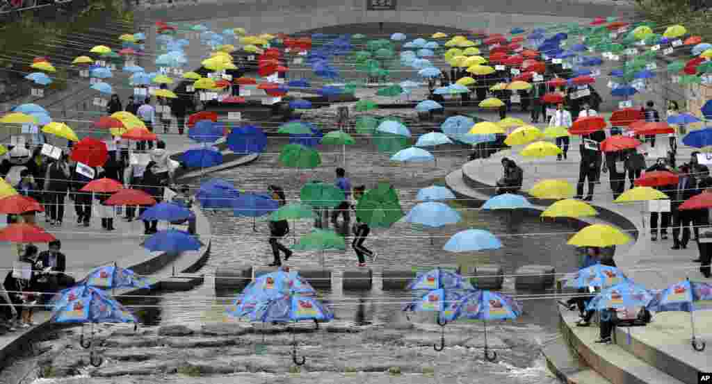 서울 청계천에 지구 환경과 평화를 상징하는 색색의 우산이 장식돼 있다. 우산 사아로 걸어다니는 사람들의 모습이 보인다.