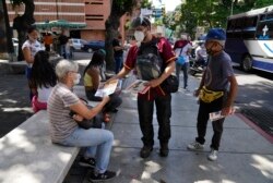 Juan Pablo Lares distributes free copies of a newspaper "Enterate" to people at a bus stop in Caracas, Venezuela, Saturday, July 31, 2021. (AP Photo/Ariana Cubillos)