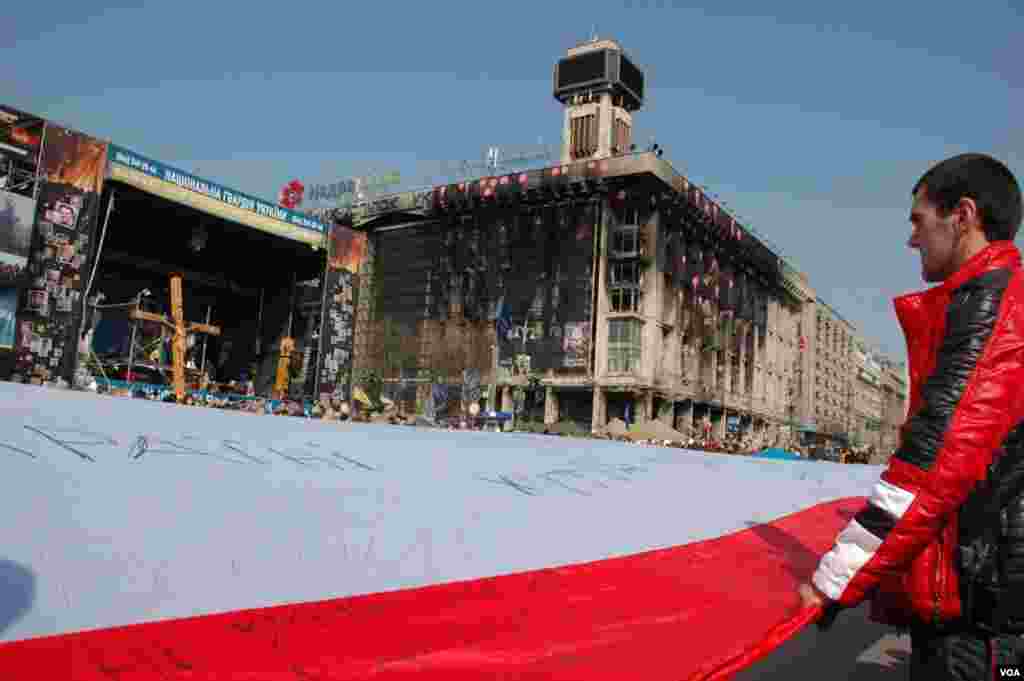 Participantes da manifestação pela unidade nacional no centro de Kiev, desenrolam uma bandeira gigante. (Steve Herman/VOA)