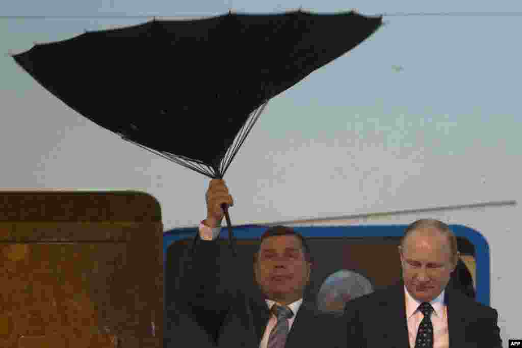 A security person struggles with an umbrella as Russia&#39;s President Vladimir Putin (R) walks out of a plane upon arriving for the fourth summit of the Conference on Interaction and Confidence Building Measures in Asia (CICA) held in Shanghai, China.
