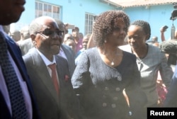 FILE - Dust engulfs former Zimbabwean president Robert Mugabe, accompanied by his wife Grace, as he arrives to vote in the general elections in Harare, Zimbabwe, July 30, 2018.