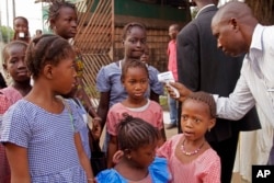 FILE - A health care worker, right, takes the temperatures of school children for signs of the Ebola virus before they enter their school in the city of Conakry, Guinea, Jan. 19, 2015.