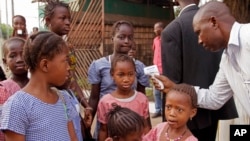 FILE - A health care worker checking for Ebola signs takes the temperatures of children before they enter their school in Conakry, Guinea, Jan. 19, 2015.