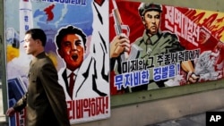 一名朝鲜人2013年3月26日在朝鲜平壤走过巨大的宣传海报，上面写着威胁惩罚“美帝国主义者和他们盟友” 的标语