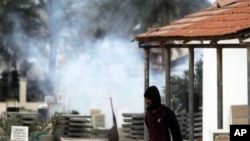 An anti-government protester carrying water to throw on tear gas canisters fired by riot police, moves through a cemetery as gas billows behind him in the Shiite Muslim village of Jidhafs, Bahrain, on the outskirts of the capital of Manama, March 17, 2011