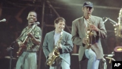 FILE - In this Aug. 16, 1991, photo, Ray Phiri, left, plays with Paul Simon, center, and actor-comedian Chevy Chase in New York's Central Park. Phiri, a South African jazz musician who founded the band Stimela and performed on Simon's "Graceland" tour, died of cancer July 12, 2017, at age 70.