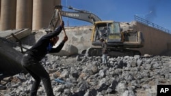 In this April 5, 2018 photo, workers remove rubble of a bridge that was destroyed last summer during fighting between U.S.-backed Syrian Democratic Forces fighters and Islamic State militants, in Raqqa, Syria. 
