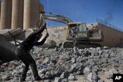 FILE - Workers remove rubble of a bridge that was destroyed last summer during fighting between U.S.-backed Syrian Democratic Forces fighters and Islamic State militants, in Raqqa, Syria, April 5, 2018.