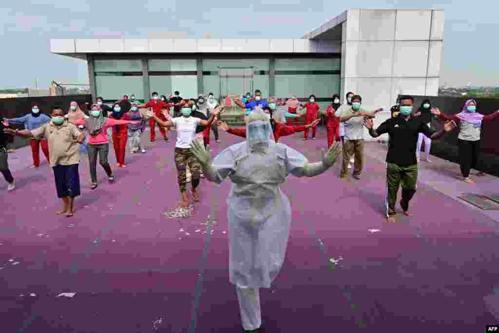 A gymnastics instructor wearing personal protective equipment (PPE) leads a morning exercise for patients of the COVID-19 coronavirus at a hotel designated to treat asymptomatic patients in Karawaci, Indonesia&#39;s Banten province.