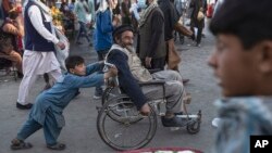 Seorang anak laki-laki tampak membantu pria dewasa yang berjalan dengan kursi roda di salah satu pasar di Kabul, Afghanistan, pada 12 Oktober 2021. (Foto: AP/Ahmad Halabisaz)