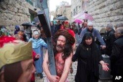 An actor dressed as Jesus Christ carries a cross as he reenacts the crucifixion walk along the Via Dolorosa towards the Church of the Holy Sepulchre, traditionally believed by many to be the site of the crucifixion of Jesus Christ, during the Good Friday procession in Jerusalem's Old City.