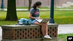 FILE - A masked student works on her laptop on the campus of Ball State University in Muncie, Ind., Sept. 10, 2020. With the spread of Omicron, many colleges are moving classes online for the first few weeks of the new year. (AP File Photo/Michael Conroy)