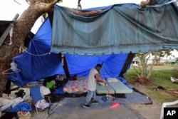 FILE - A resident sweeps at a camp set up on the shore of Laguna de Condado in San Juan, Puerto Rico, Oct. 23, 2017.