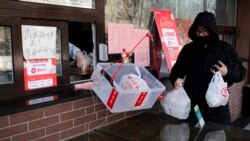 Un hombre recoge bolsas de su pedido de alimentos mientras un trabajador lo coloca en una canasta para evitar el contacto humano después del brote de coronavirus, en Beijing, el domingo 23 de febrero de 2020.