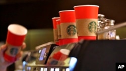 A barista reaches for a red paper cup as more, with cardboard liners already attached, line the top of an espresso machine at a Starbucks coffee shop in the Pike Place Market in Seattle, Nov. 10, 2015.