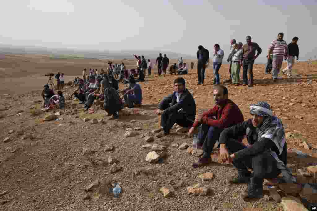 People gather on a hilltop on the outskirts of Suruc to watch fighting between Syrian Kurds and the militants of Islamic State group in Kobani, Syria, Oct. 13, 2014.