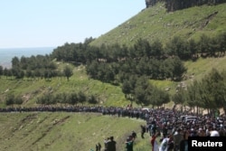 FILE - People gather near the headquarters of the Kurdish People's Protection Units (YPG) after it was hit by Turkish airstrikes in Mount Karachok near Malikiya, Syria, April 25, 2017.