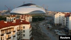 Workmen walk through the under construction Olympic Village, which sits in front of the Bolshoy Ice Dome on the Olympic Park for the Sochi 2014 Winter Olympic Games, in Adler, Russia, Aug. 19, 2013. 