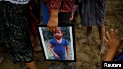 FILE - A man holds a picture of Jakelin Caal, 7, during her funeral at her home village of San Antonio Secortez, in Guatemala, Dec. 25, 2018.