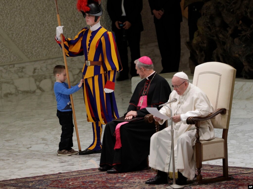 바티칸&nbsp;바오로 6세 알현실에서 프란치스코 교황이 연설하는 도중 어린 소년이 경비대원의 옷을 만지고 있다.
