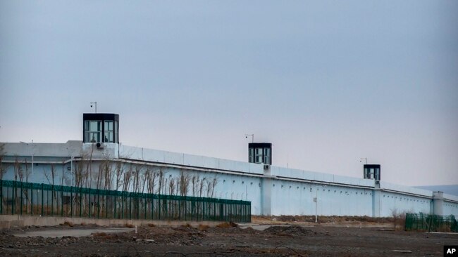 People stand watching the enclosing wall of the Urumqi No. 3 Detention Center in Dabancheng in western China's Xinjiang Uyghur Autonomous Region on April 23, 2021 where many Uyghurs are detained, some mothers for having too many children. (AP Photo/Mark Schiefelbein)