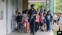 A Santa Monica police officer leads children on a field trip out of Santa Monica College, where they had gone for a planetarium show, following a shooting in the area, in Santa Monica, California, June 7, 2013.