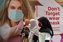 Sejumlah perempuan bermasker melewati iklan yang mempromosikan kesadaran akan wabah virus corona di sebuah pusat perbelanjaan di Jakarta, Rabu, 1 Juli 2020. (Foto: AP/Tatan Syuflana)