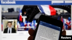 An illustration photo shows the message of former French President Nicolas Sarkozy on his Facebook page displayed on a mobile phone internet browser held in front of a computer screen which also displays his Facebook page in Paris, Sept. 19, 2014. 