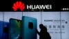 FILE - A woman browses her smartphone as she walks by a Huawei store at a shopping mall in Beijing, Dec. 11, 2018. 