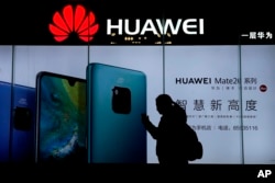 FILE - A woman browses her smartphone as she walks by a Huawei store at a shopping mall in Beijing, Dec. 11, 2018.