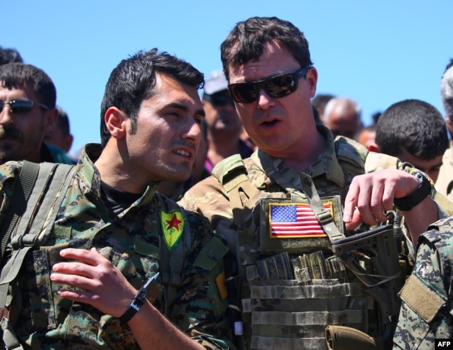 FILE - A U.S. officer from the U.S.-led coalition speaks with a fighter from the Kurdish People's Protection Units (YPG) at the site of Turkish airstrikes near the northeastern Syrian Kurdish town of Derik, April 25, 2017.