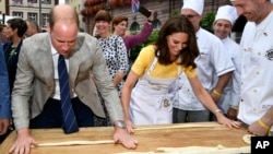 Andreas Goebes of the bakers guild Heidelberg, right, watches as Britain's Prince William, left, and Princess Kate, form dough into pretzels during their visit of the market in the historic center of the German city of Heidelberg, July 20, 2017.